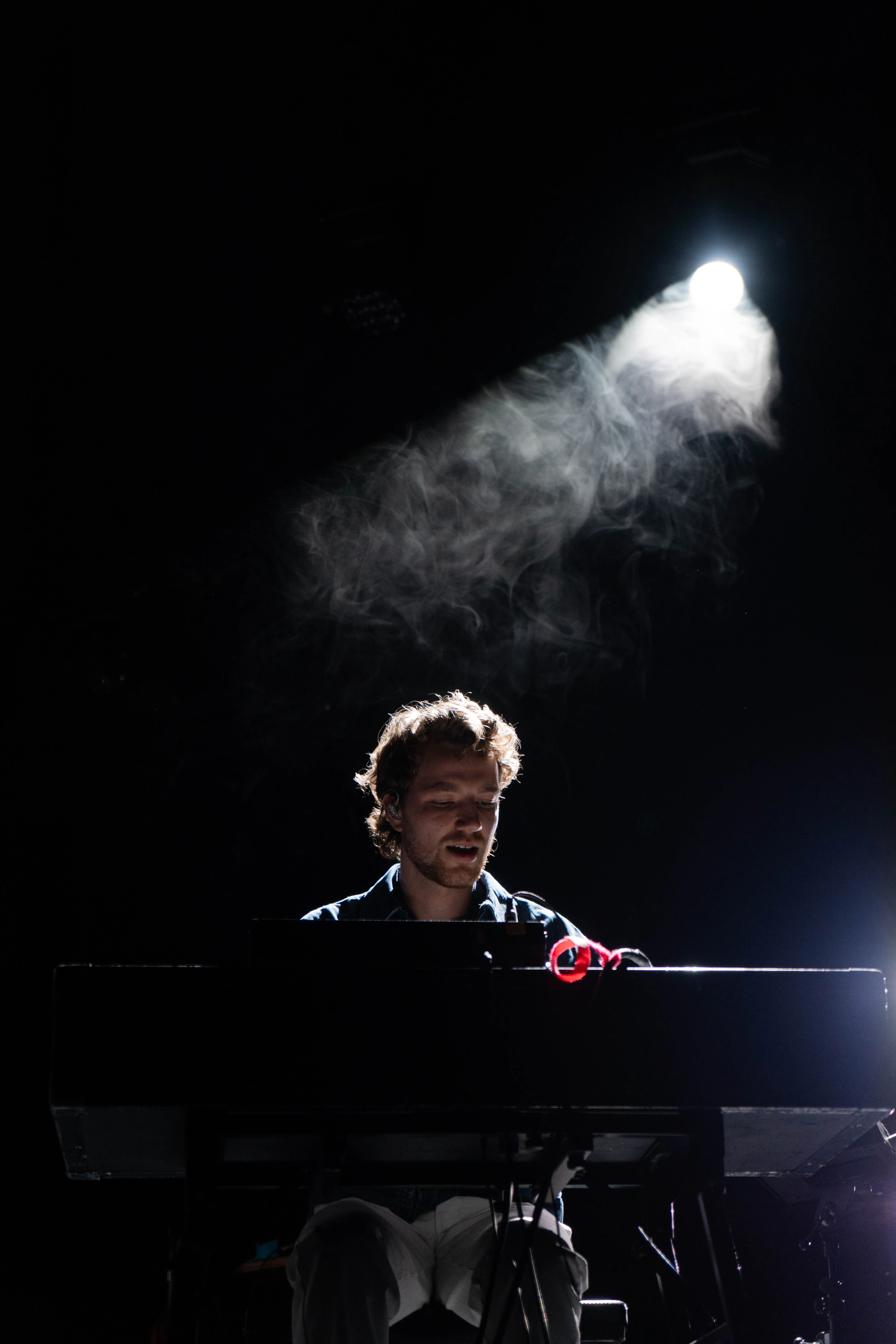 Een muzikant speelt op een piano, terwijl een lichte nevel en een spotlicht de sfeer benadrukken.
