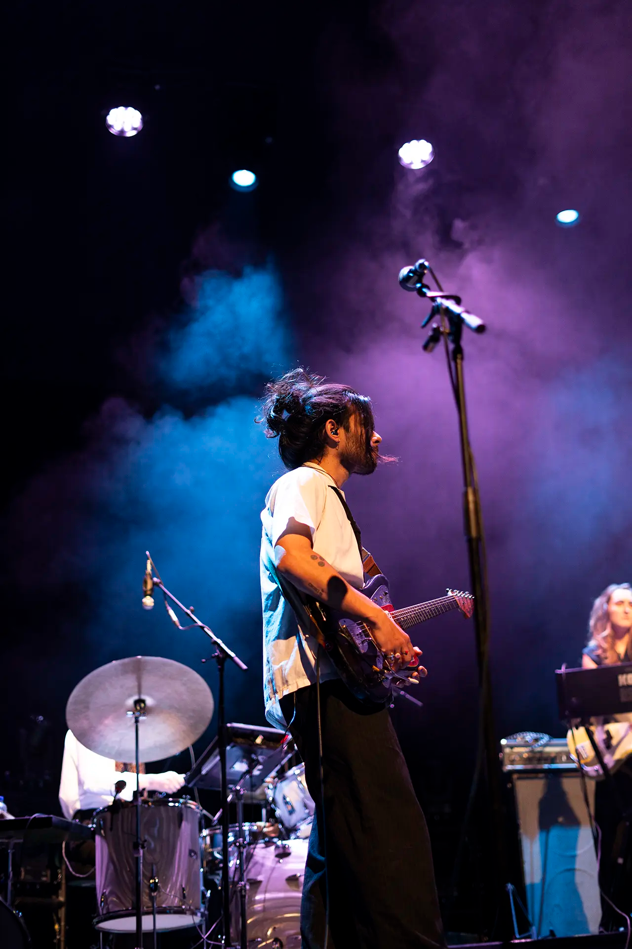 Een muzikant speelt gitaar op het podium terwijl sfeervolle verlichting en rook effect aan de performance toevoegen.